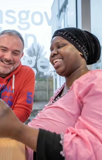 Lecturer in an orange hoodie and a student in a pink top smiling while working together on assembling a blue robotic vehicle near a large window with Glasgow Kelvin College branding Lecturer in an orange hoodie and a student in a pink top smiling while working together on assembling a blue robotic vehicle near a large window with Glasgow Kelvin College branding
